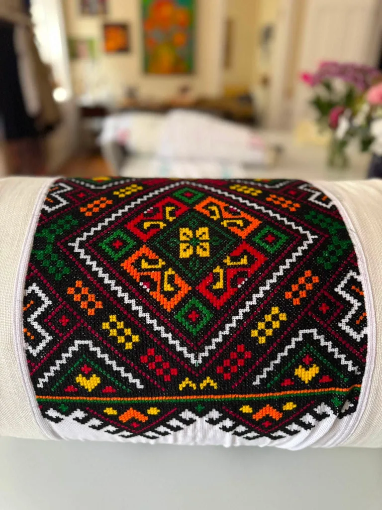 A geometric Hutsul cross-stitch cushion in red, green, yellow and black on white linen.