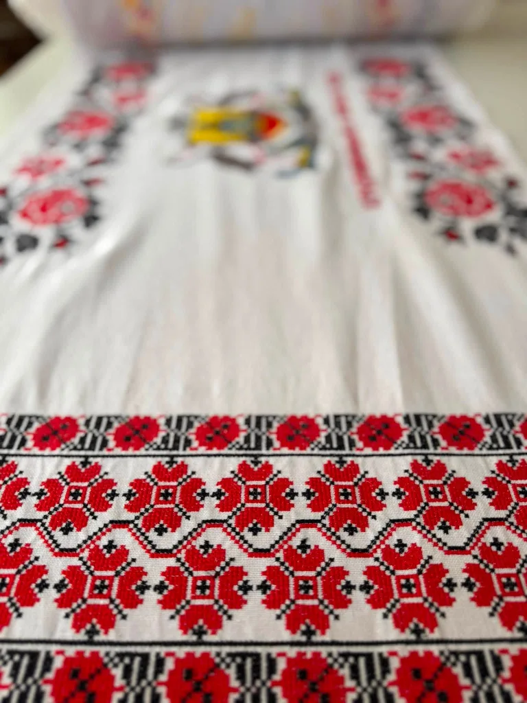 A red cross-stitch rushnyk with a poppy border on white linen.