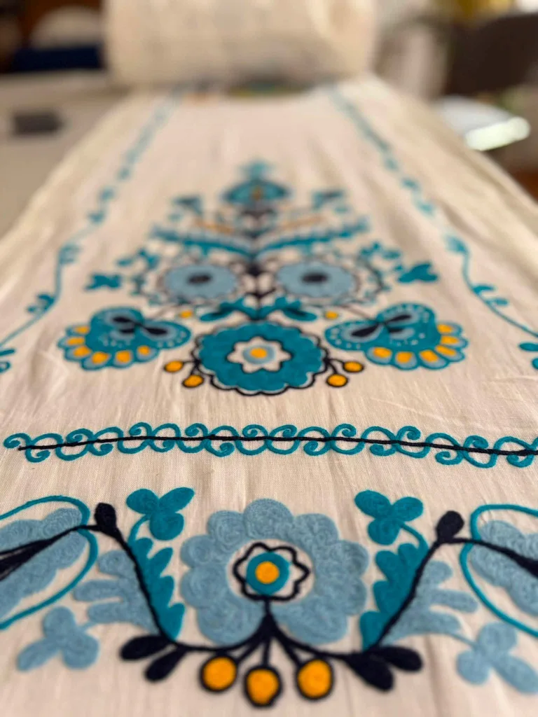 Turquoise and blue floral crewel embroidery on a white runner.