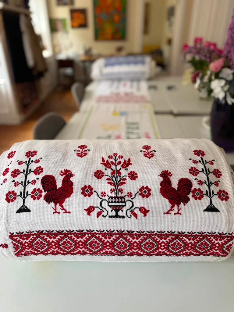 A red and black cross-stitch rushnyk with roosters and a flowering tree.