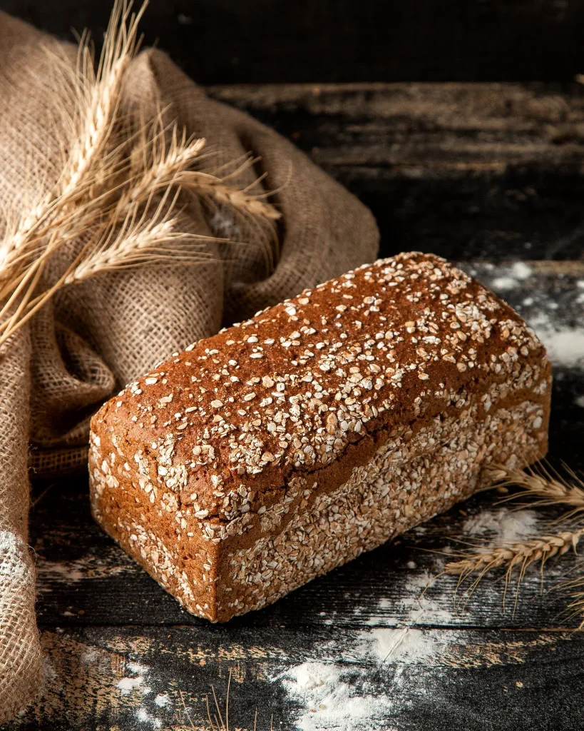 A seeded loaf on sacking, with ears of wheat behind it.