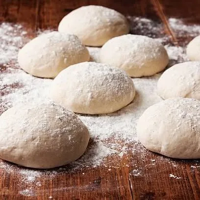 Rounds of risen dough dusted with flour on a dark wooden board.