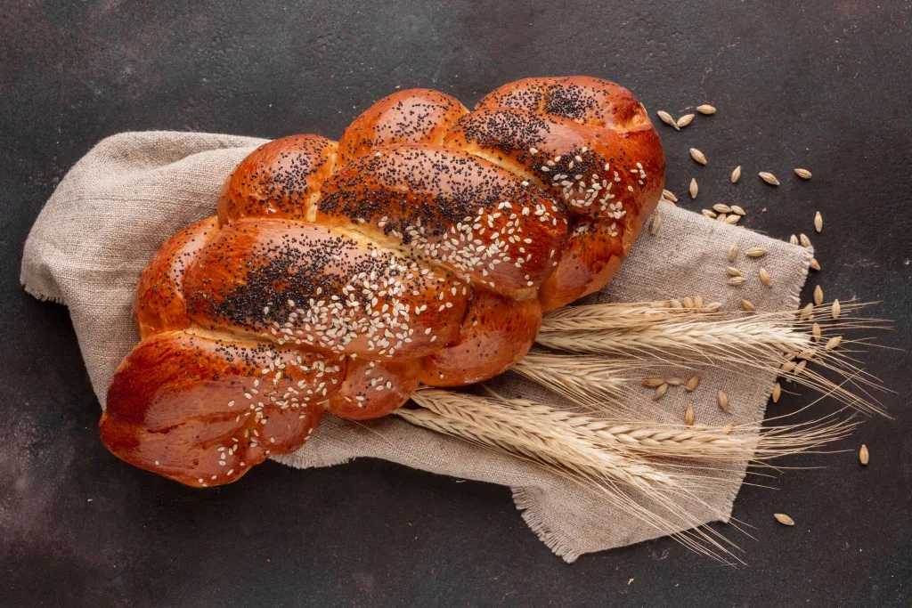 A plaited loaf topped with poppy seeds, on linen with ears of wheat.