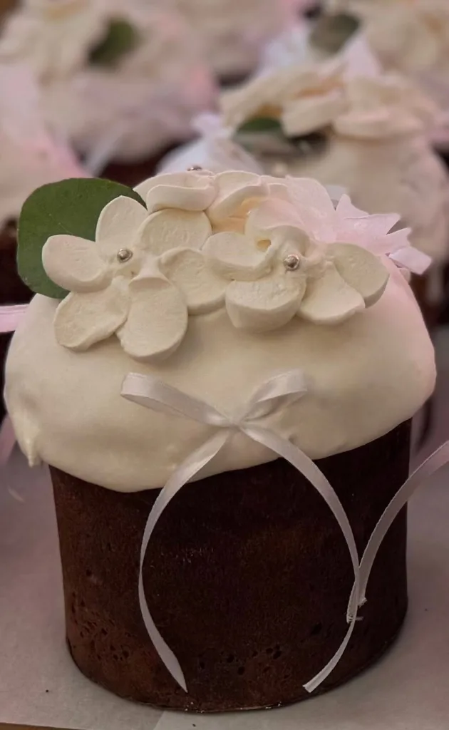 An Easter bread under white icing, topped with sugar flowers and a ribbon.