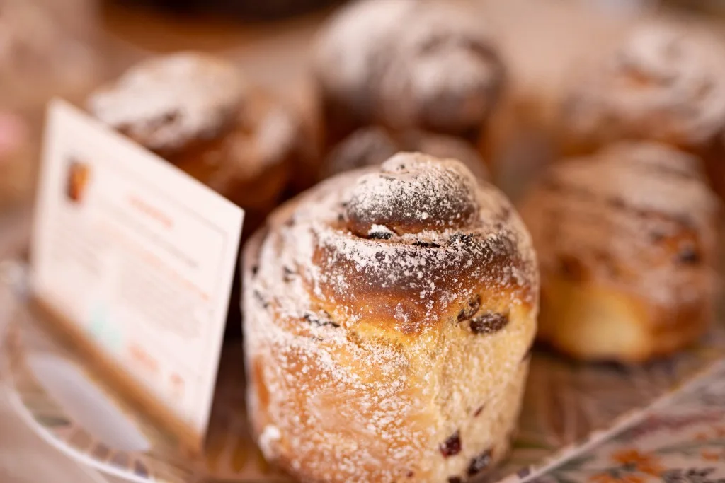 A sugar-dusted Easter bread in close-up, with more behind it and a price card.
