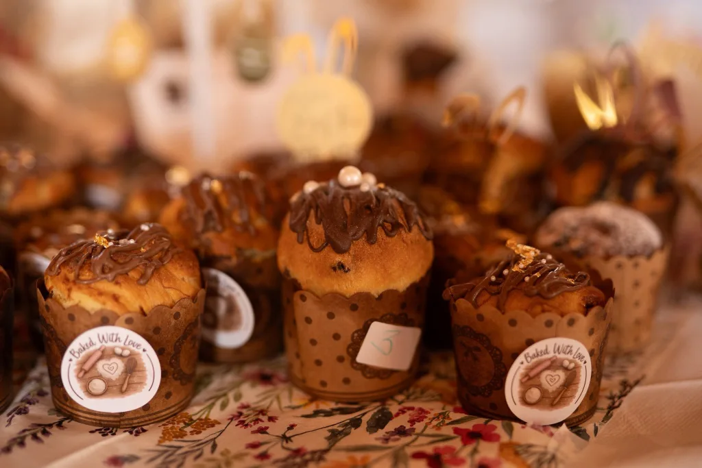 Rows of small Easter breads in paper cases on a patterned cloth at a stall.
