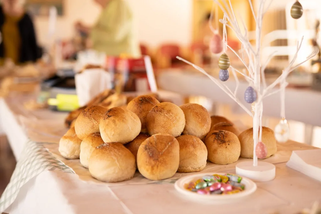 A table of small round rolls beside a white decorated branch and sugared almonds.