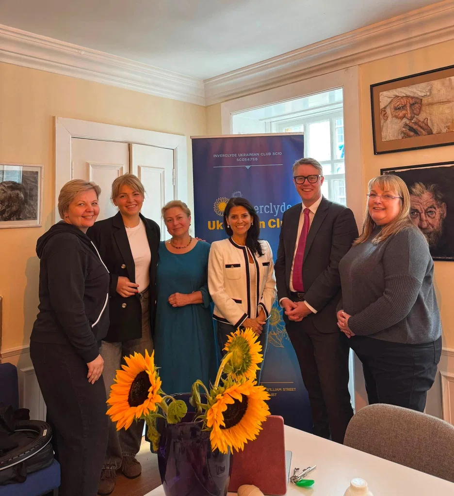 Members of the Inverclyde Ukrainian Club welcoming guests at Dutch Gable House, in front of the Club banner, with sunflowers on the table