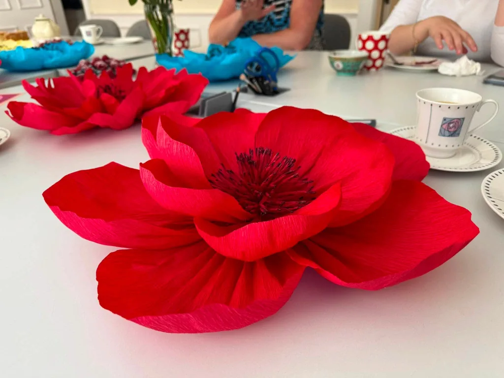 Large red crepe-paper poppies made in a Club craft workshop, on a table with coffee cups