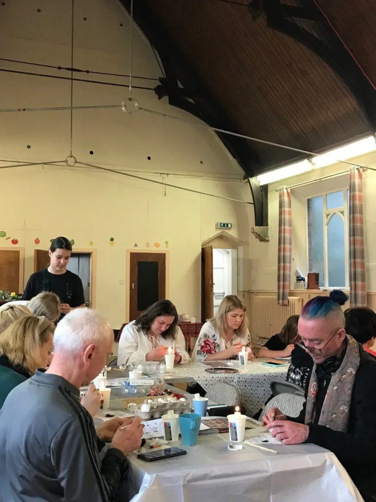 People at tables across the hall, each working on an egg.
