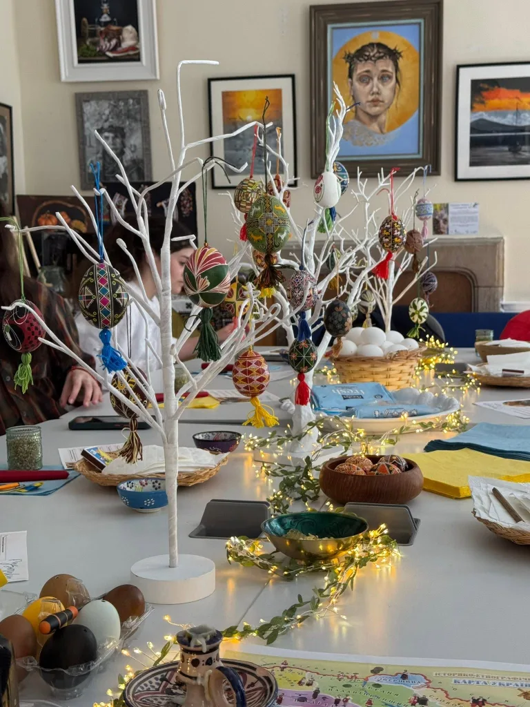 White decorative trees hung with pysanky, in a room with pictures on the wall.