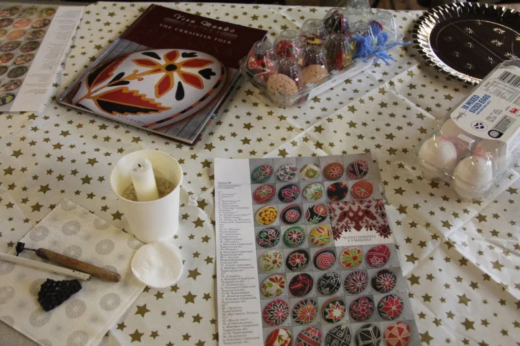 A workspace seen from above: a pattern book, a candle, a kistka, blank eggs and an instruction sheet.
