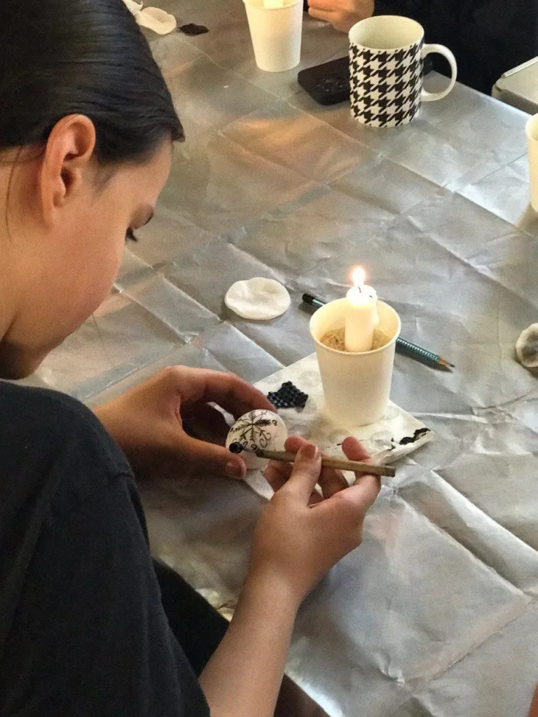 A woman drawing on an egg over a candle at a table.